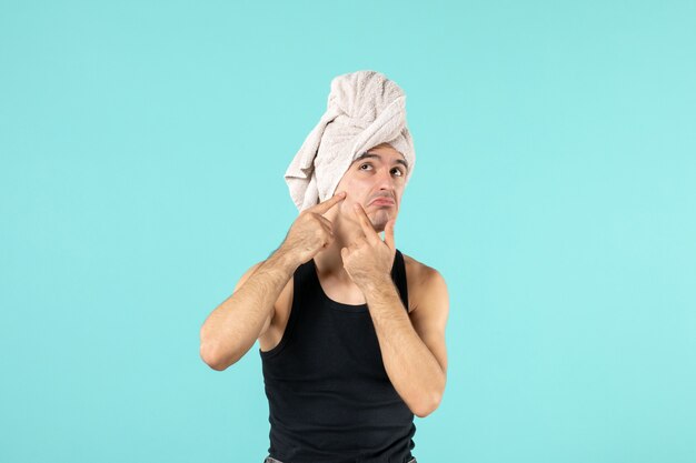 front view of young man after shower trying to squeeze out little pimple on blue wall