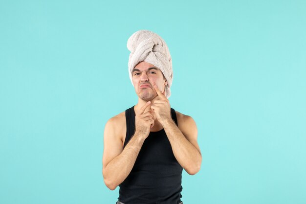 front view of young man after shower trying to squeeze out little pimple on blue wall