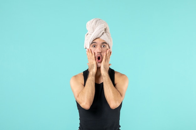 front view of young man after shower with towel on his head on blue wall