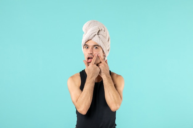 Front view of young man after shower with towel on his head on blue wall