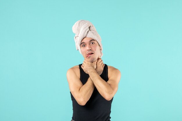 front view of young man after shower with towel on his head chucking himself on blue wall