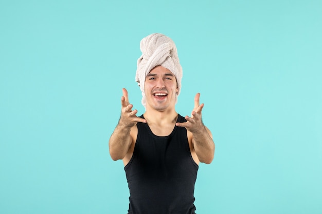 front view of young man after shower with towel on his head crying on blue wall