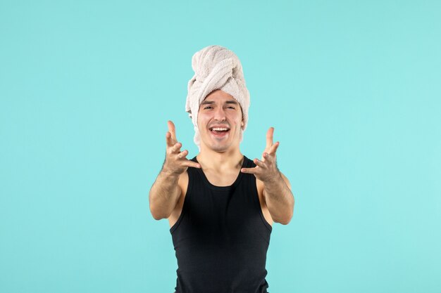 front view of young man after shower with towel on his head crying on blue wall