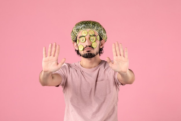 вид спереди молодого человека, применяющего маску из огурца на лице на розовой стене