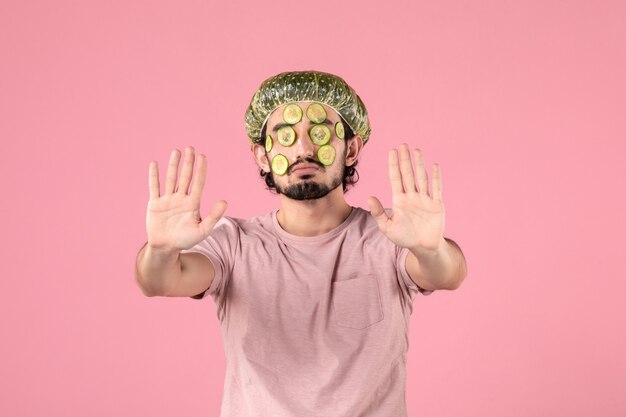 front view of young man applying cucumber mask on his face on pink wall