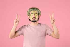 Free photo front view of young man applying cucumber mask on his face on pink wall