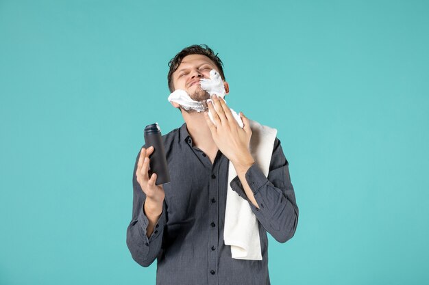 青い壁に彼の顔に剃るために泡を適用する若い男の正面図