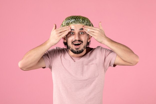 front view of young man applying mask on his face on pink wall