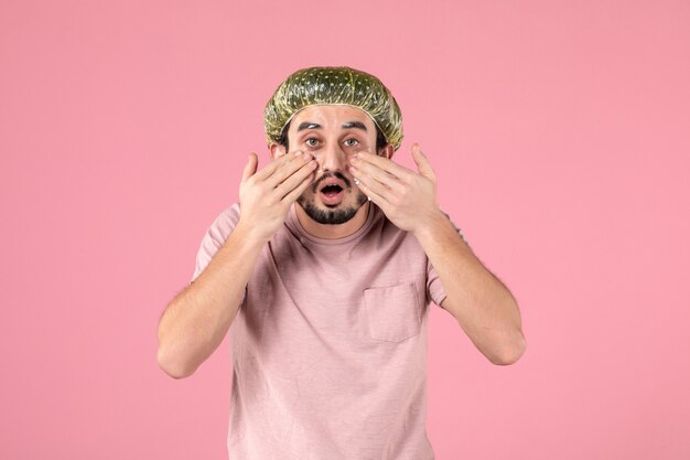 front view of young man applying mask on his face on pink wall