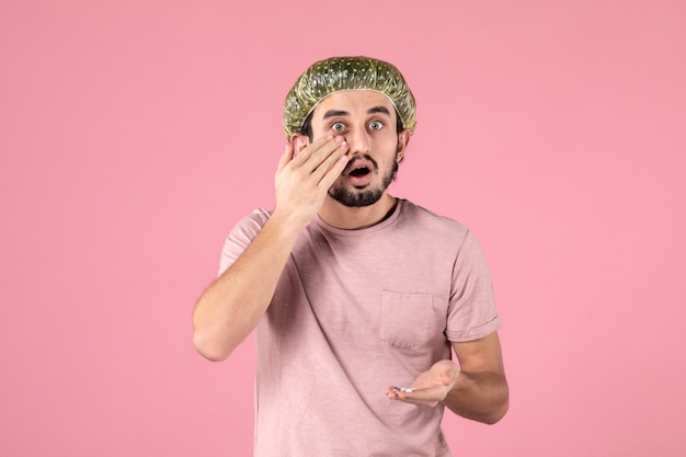 front view of young man applying mask on his face on pink wall