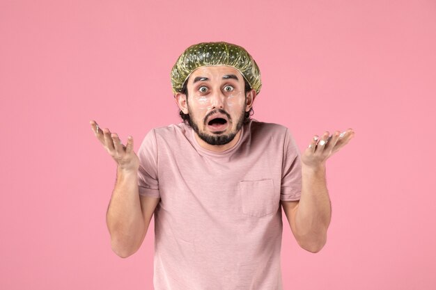 вид спереди молодого человека, применяющего маску на лице на розовой стене