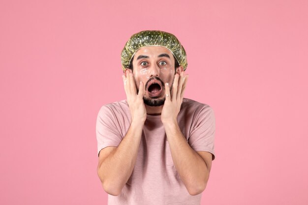 front view of young man applying mask on his face on pink wall