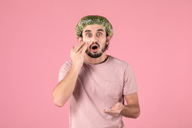 front view of young man applying mask on his face on pink wall
