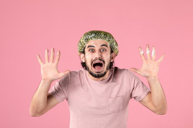 front view of young man applying mask on his face on pink wall