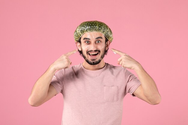 front view of young man applying mask on his face on pink wall