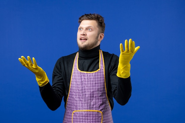 Front view of young man in apron standing on blue wall