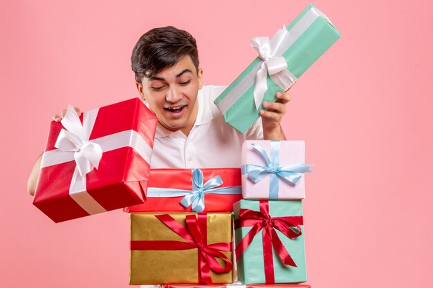 Front view of young man around christmas presents on pink wall