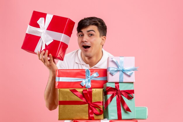 Front view of young man around christmas presents on pink wall