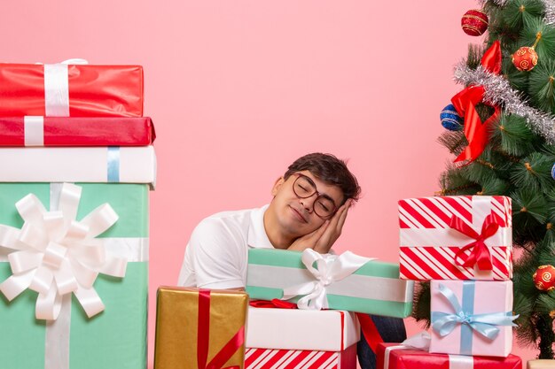 Front view of young man around presents and christmas tree on a pink wall