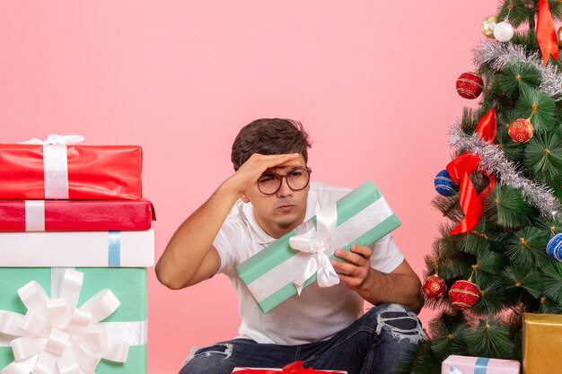 분홍색 벽에 선물과 크리스마스 트리 주위에 젊은 남자의 전면보기