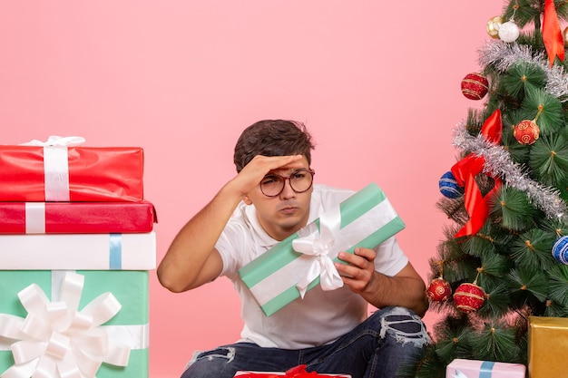 Front view of young man around presents and christmas tree on a pink wall