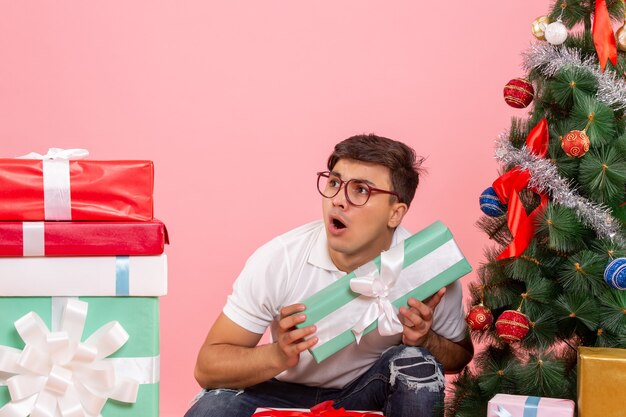 Front view of young man around presents and christmas tree on pink wall