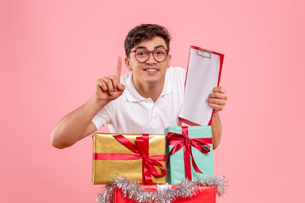 クリスマスの周りの若い男の正面図はピンクの壁に笑みを浮かべてファイルノートを保持している