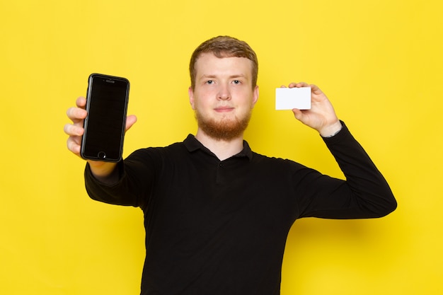 Front view of young man in black shirt holding card and phone