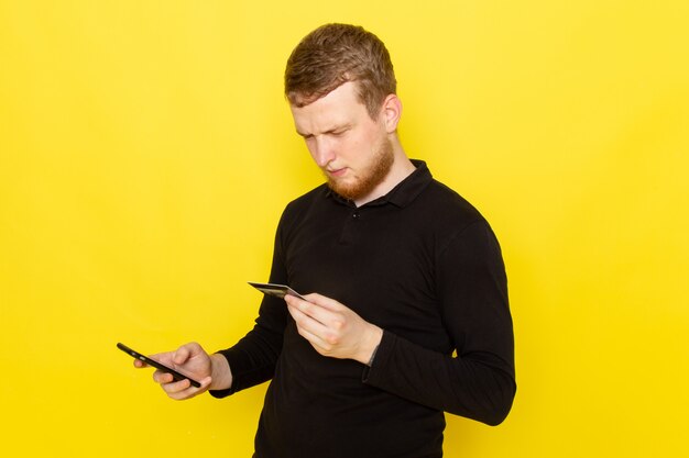 Front view of young man in black shirt holding card and using a phone