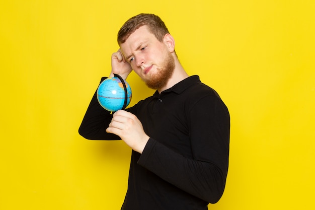 Front view of young man in black shirt holding little globe and thinking