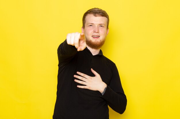 Front view of young man in black shirt posing pointing out and laughing