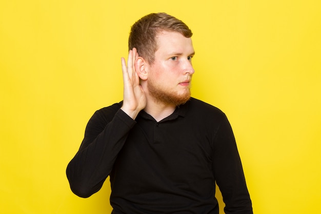 Front view of young man in black shirt posing and trying to hear out