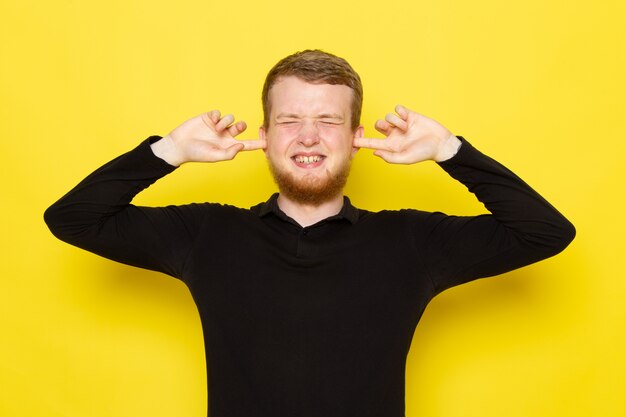 Front view of young man in black shirt posing while stucking his ears