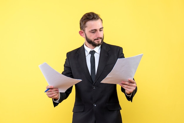 Front view of young man in black suit checking documents on yellow