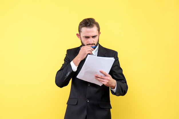 Front view of young man in black suit concentrating to the blank document on yellow wall