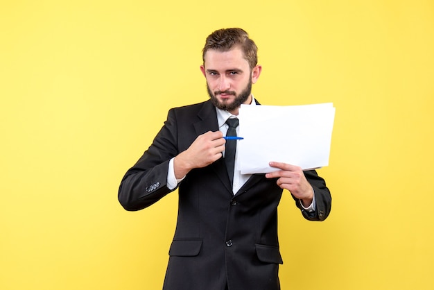 Vista frontale del giovane in abito nero che punta con sicurezza con una penna sul documento in bianco su giallo