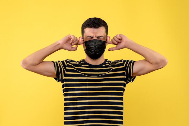 Free photo front view young man in black and white striped t-shirt closing his ears on yellow background