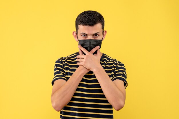 Front view young man in black and white striped t-shirt holding chin yellow isolated background