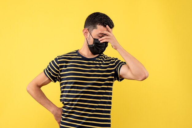 Front view young man in black and white striped t-shirt holding head on yellow background