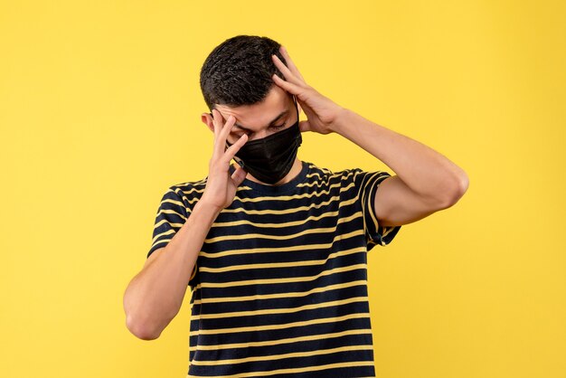 Front view young man in black and white striped t-shirt holding head yellow background