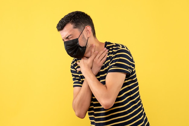 Front view young man in black and white striped t-shirt holding his throat with pain on yellow background