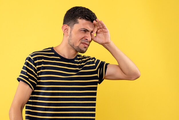 黄色の孤立した背景に何かを見ている黒と白の縞模様のTシャツの正面図若い男