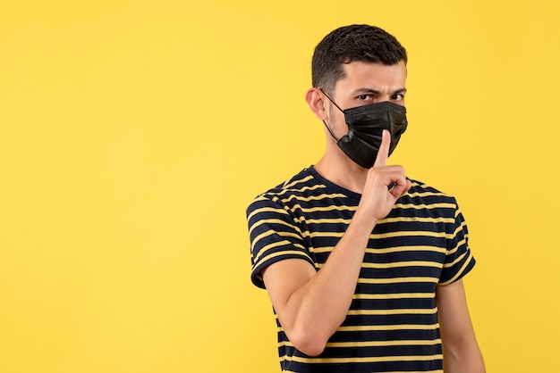 Front view young man in black and white striped t-shirt making shh sign on yellow background