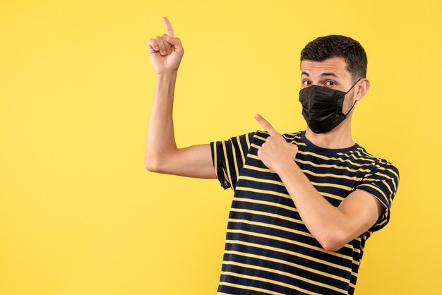 Front view young man in black and white striped t-shirt pointing at back yellow background