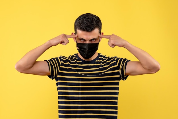 Front view young man in black and white striped t-shirt putting fingers on his temple on yellow background