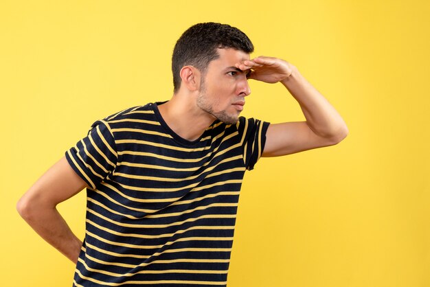 Front view young man in black and white striped t-shirt putting hand to forehead on yellow isolated background