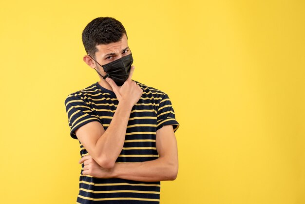 Front view young man in black and white striped t-shirt putting hand on his chin yellow background