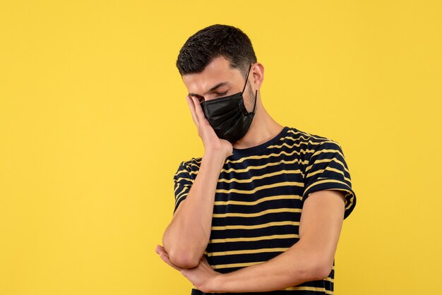 Front view young man in black and white striped t-shirt putting hand on his face yellow background