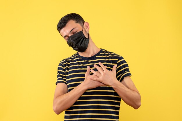 Front view young man in black and white striped t-shirt putting hands on his chest yellow background