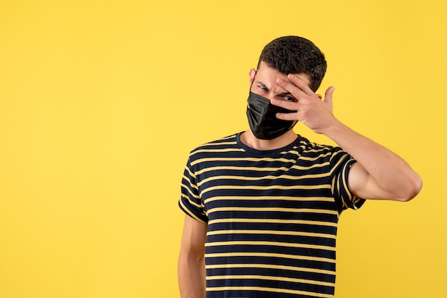 Front view young man in black and white striped t-shirt standing on yellow background copy place